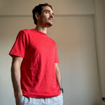 Engine Red | Man wearing a red t-shirt and light gray pants standing against a plain wall.