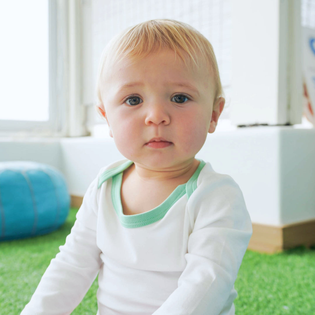 Baby wearing long sleeve bodysuit in white with grass green made with peruvian pima cotton