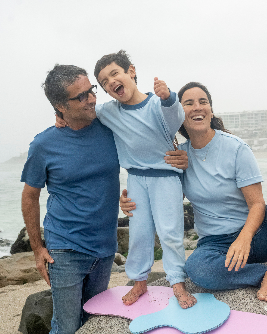 Light Blue | Family of three standing on a beach with a child on a pink and blue float.