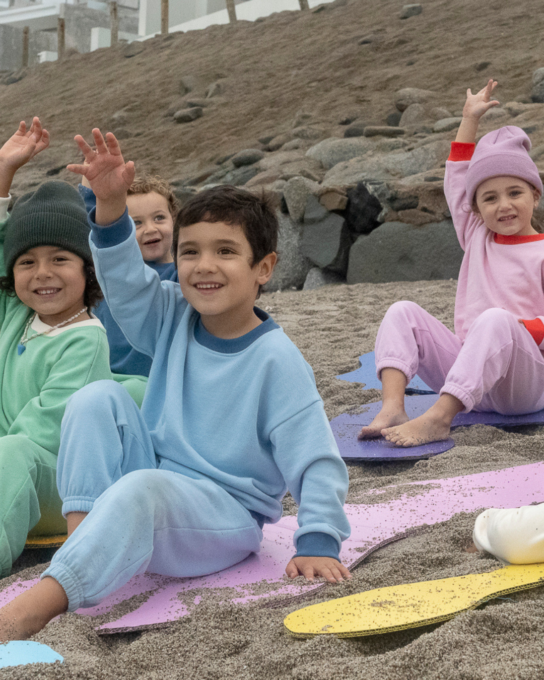 Light Blue; Pink; Grass Green | Children sitting on colorful mats in a sand pit with rocks in the background