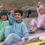Light Blue; Pink; Grass Green | Children sitting on colorful mats in a sand pit with rocks in the background