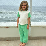 Grass Green | Child wearing a green and white outfit standing by a fence with ocean view