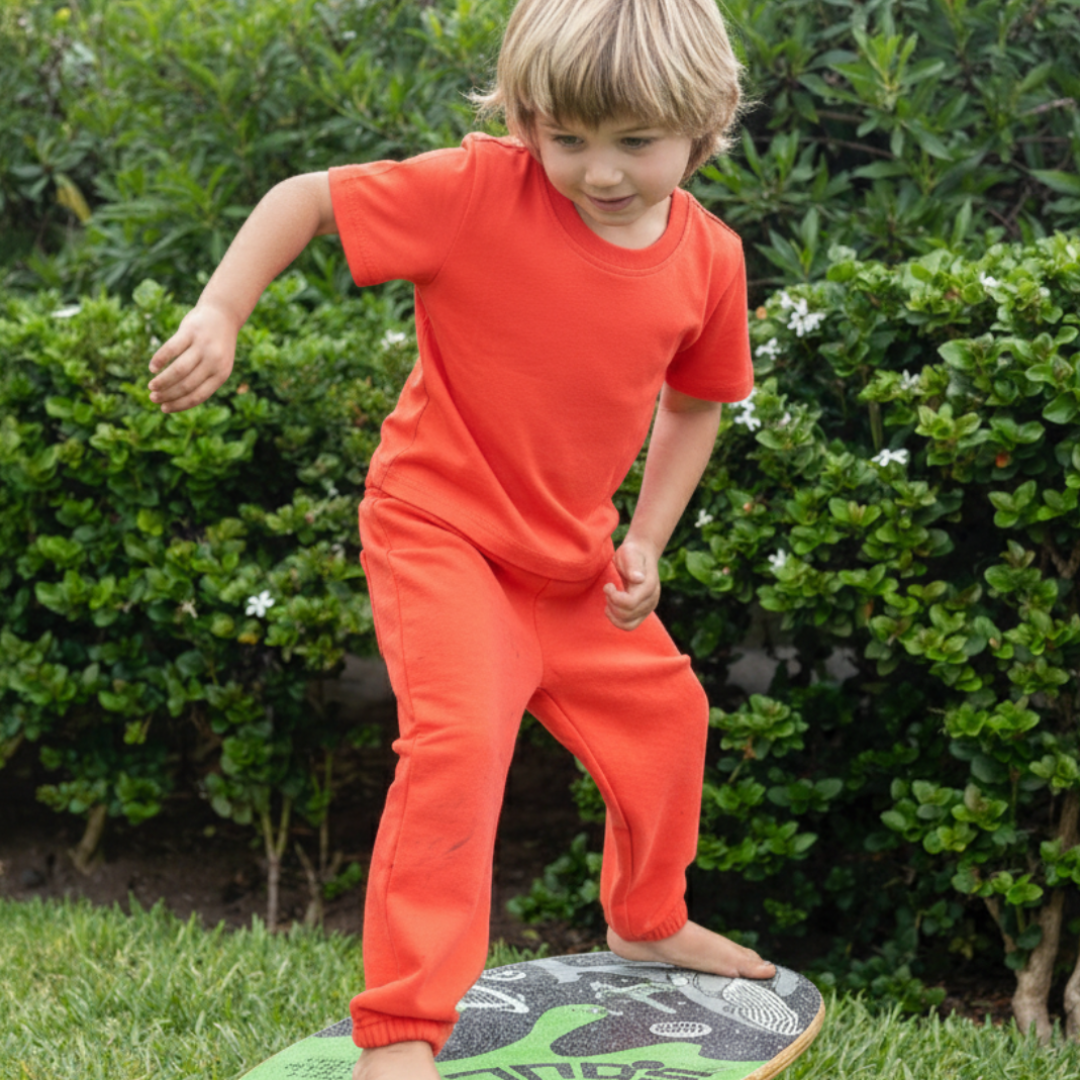 Engine Red | Child in red outfit standing on a green balance board outdoors.
