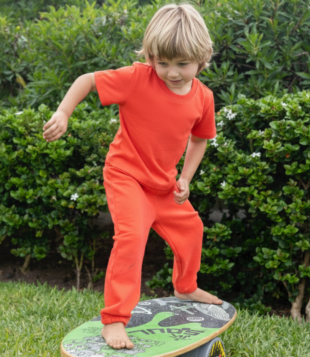 Engine Red | Child in red outfit standing on a green balance board outdoors.
