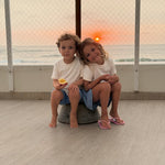 White | Two children sitting on a rock by a window with a sunset view of the ocean.