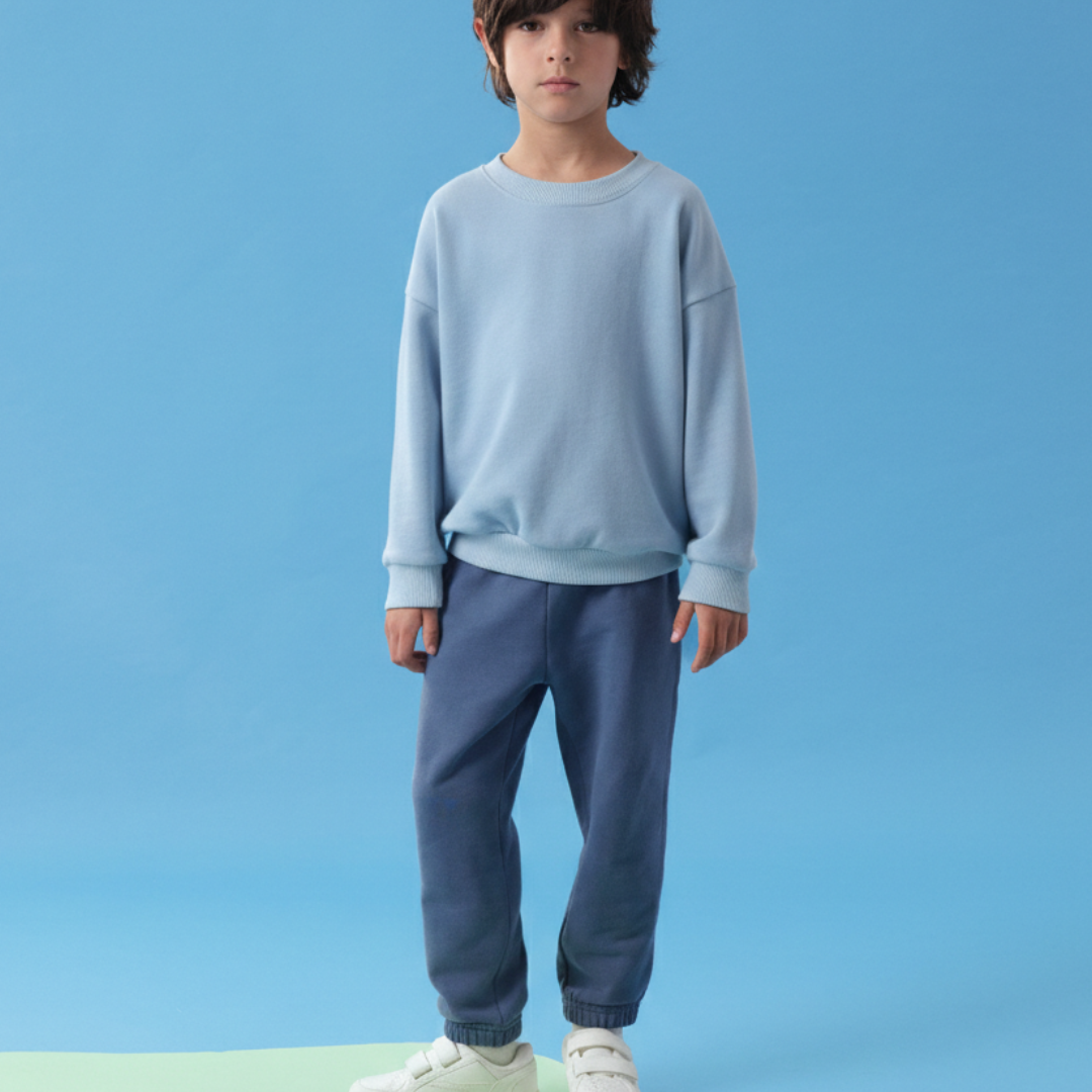 Light Blue | Child wearing a light blue sweatshirt and dark blue pants on a solid blue background