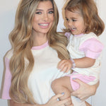 White with Pink| Woman holding a child both wearing matching pink and white outfits against a plain background