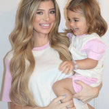 White with Pink| Woman holding a child both wearing matching pink and white outfits against a plain background