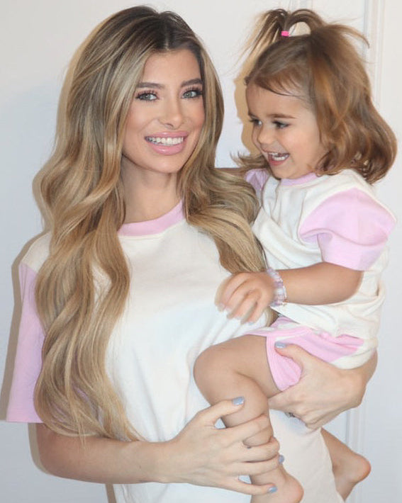 White with Pink| Woman holding a child both wearing matching pink and white outfits against a plain background