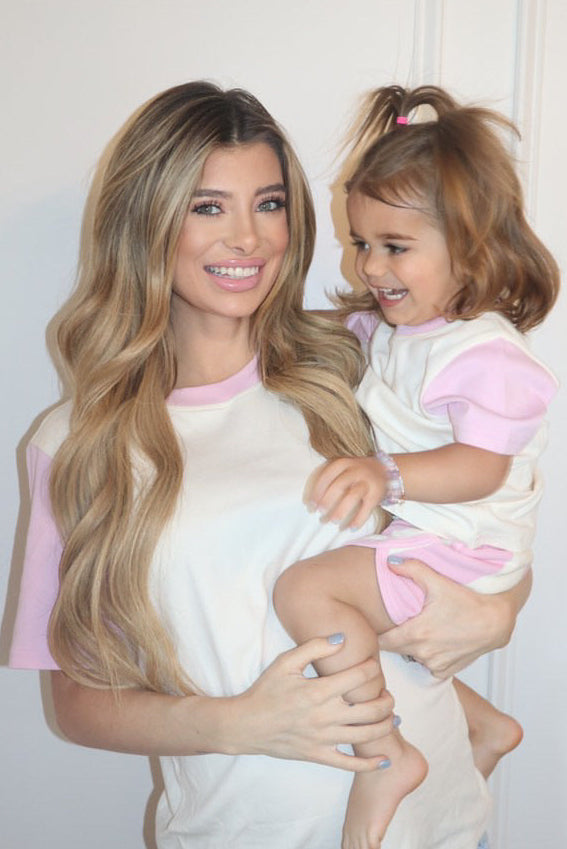 White with Pink| Woman holding a child both wearing matching pink and white outfits against a plain background