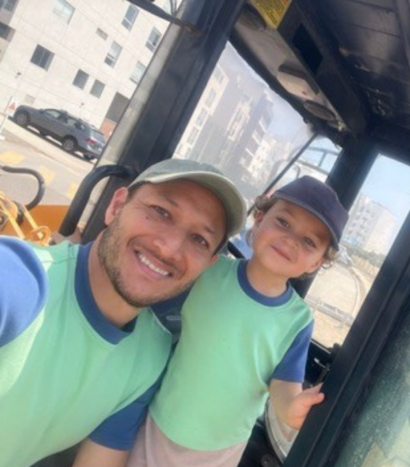 Grass Green with Navy Blue | Man and child in matching green and blue shirts inside a vehicle with cityscape background