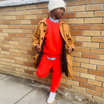 Engine Red | Kid wearing a red outfit with a tan coat against a brick wall.