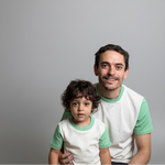 White with Green Grass | Man and child in matching green and white shirts sitting together in a room.