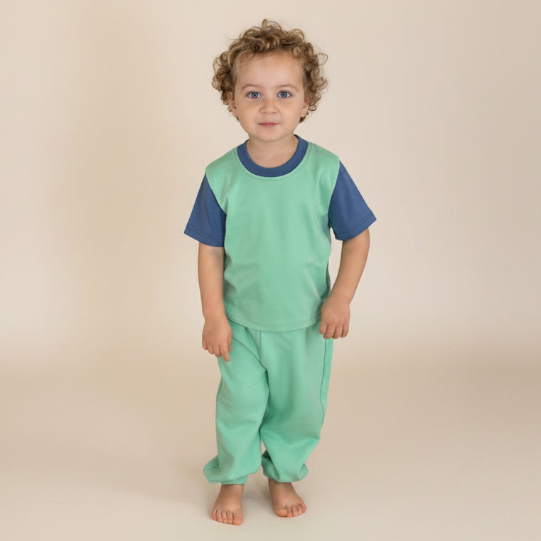 Grass Green with Navy Blue | Child wearing a green outfit standing on wooden stairs