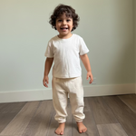 White | Child wearing a white t-shirt and cream pants standing on a wooden floor.